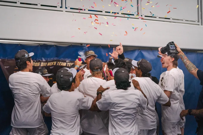 A group of athletes huddle together in celebration, confetti falling above them. They are wearing matching caps and white shirts. One team member is taking a picture, banner reads \"2026 DIII MEN'S TEAM TEX\".