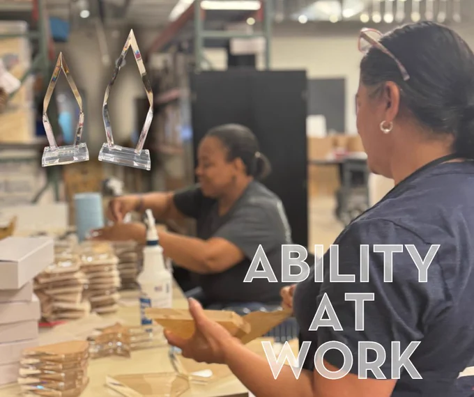 Two women assembling wooden pieces in a workshop with stacks of materials and the text 'ABILITY AT WORK' overlayed.