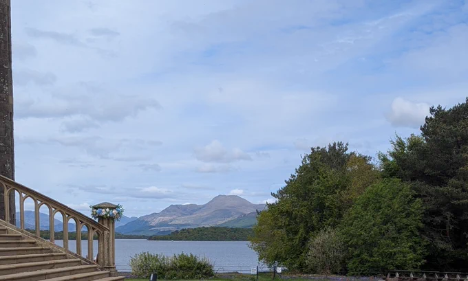 Ben Lomond seen from the drive of Ross Priory. The bottom of the steps has a wedding wreath. Green trees to the right, blue cloudy sky over the mountain