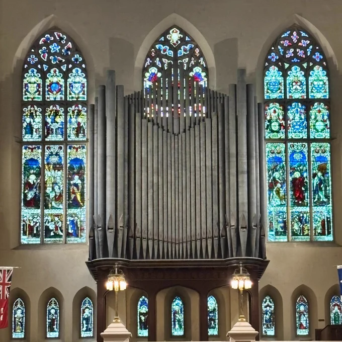 Large pipe organ centered between three tall stained glass windows inside a church interior.