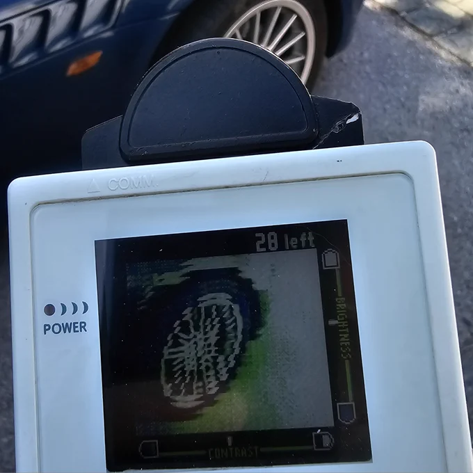 Ein Game Boy Color mit Game Boy Kamera auf einen Autoreifen gerichtet. Am Display des Game Boys sind Bildfehler zu sehen. 