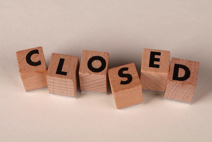 Wooden blocks spell 'closed' on a beige background, symbolizing closure or shut down.