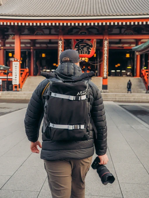 A traveler with a backpack and camera approaches a traditional temple. The scene evokes a sense of adventure and exploration.