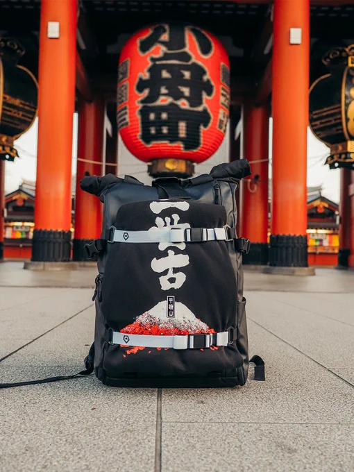 A black backpack with Japanese lettering and Mt. Fuji design is displayed in front of a large red lantern at a Japanese temple, capturing a blend of modern style and traditional culture.