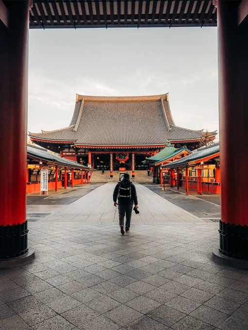 A lone traveler walks towards a traditional Japanese temple at dusk. The scene captures a sense of serenity and exploration in a historic setting.