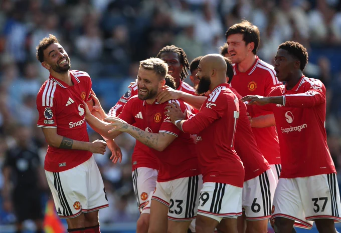 Manchester United players in red jerseys celebrate together on the pitch during a match, showing team unity and excitement towards Bruno Fernandes.