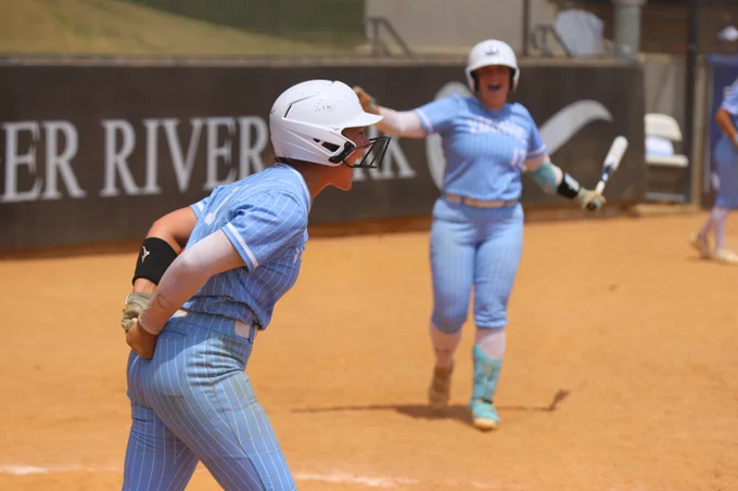 Two softball players celebrate on the field.