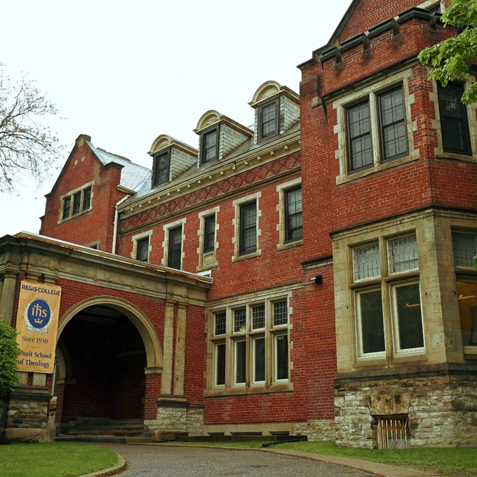 Historic red brick building with arched entrance and stone foundation surrounded by greenery.