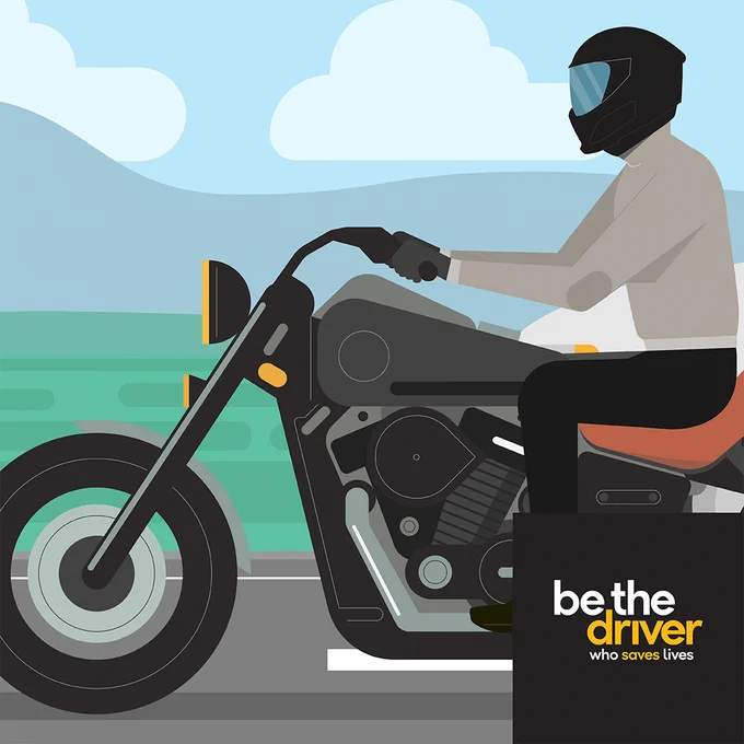 Graphic of the profile of a motorcyclist wearing a helmet and riding gear in traffic. Bold text reads, “Be the driver." Background uses simplified roadside visuals of hills and grass. 