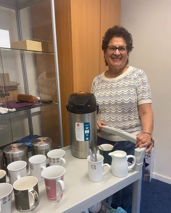Volunteer Joan with a tea and coffee tray smiling brightly.