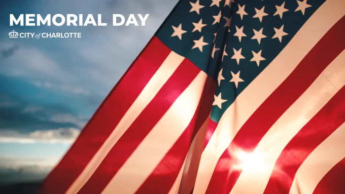 An American flag waving in the breeze against a cloudy sky. The text reads "Memorial Day" next to the "City of Charlotte" logo.