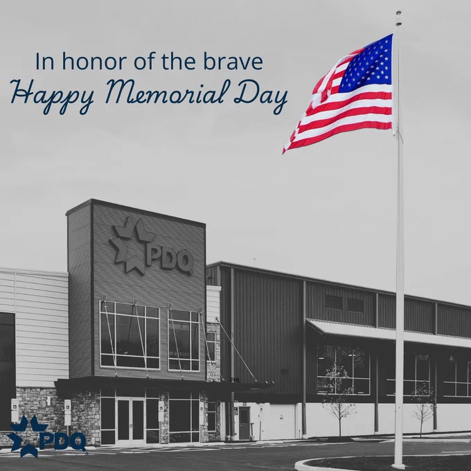 Black and white PDQ restaurant exterior with a colorful American flag flying out front. Text reads: "In honor of the brave, Happy Memorial Day."