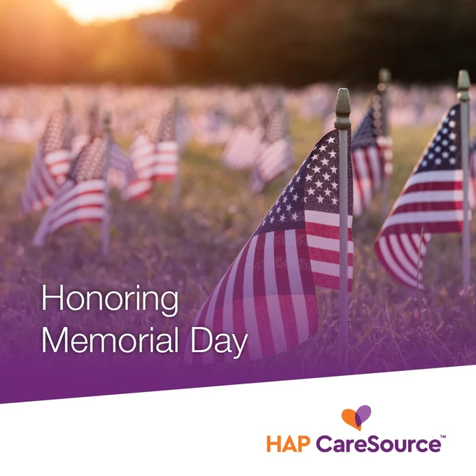 A field filled with American flags is shown in the background, symbolizing Memorial Day. The text "Honoring Memorial Day" appears in the foreground, with the HAP CareSource logo beneath it. Sunlight is visible in the distance.