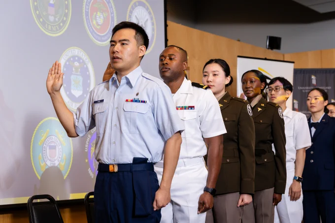 A diverse group of military personnel in uniform stands in a line, raising their right hands during a formal oath ceremony.