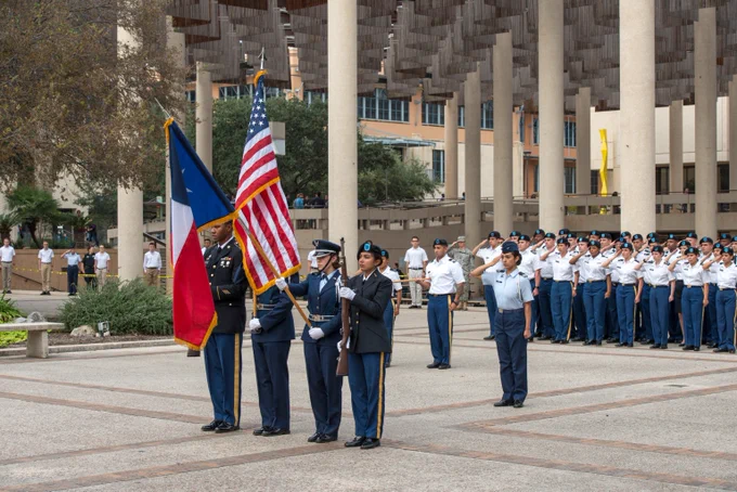 Military personnel in uniform presenting the Texas and American flags during a formal outdoor ceremony.