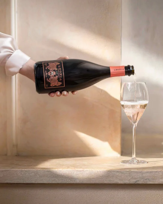 Still life of a dark wine bottle resting on a light stone surface beside a filled white wine glass, bottle of Leonia Rosé Metodo Classico label with Marchesi Frescobaldi branding visible, elegant winery lifestyle image.