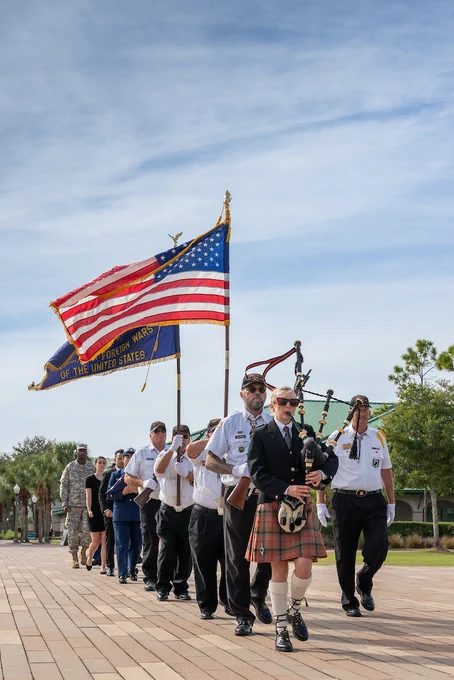 a photo of people walking down the library lawn in a procession with an American flag