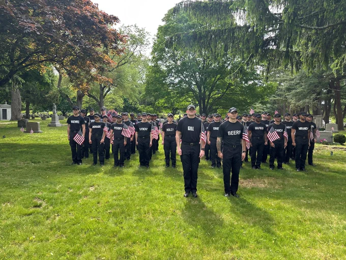 Student officers standing solemnly on green grass with American flags in hand.
