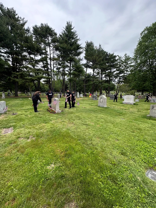 Student officers placing American flags near headstones in a cemetery.