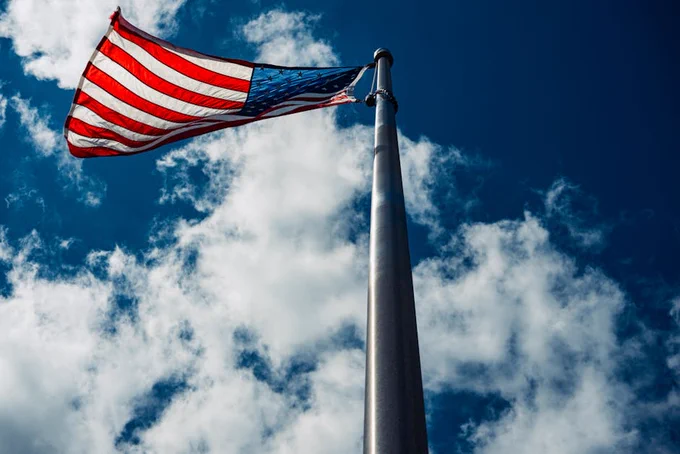 Low angle view of an American flag waving against a bright blue sky with clouds.
