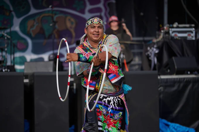 Performer in vibrant traditional attire skillfully twirling two hoops on stage during a cultural dance.