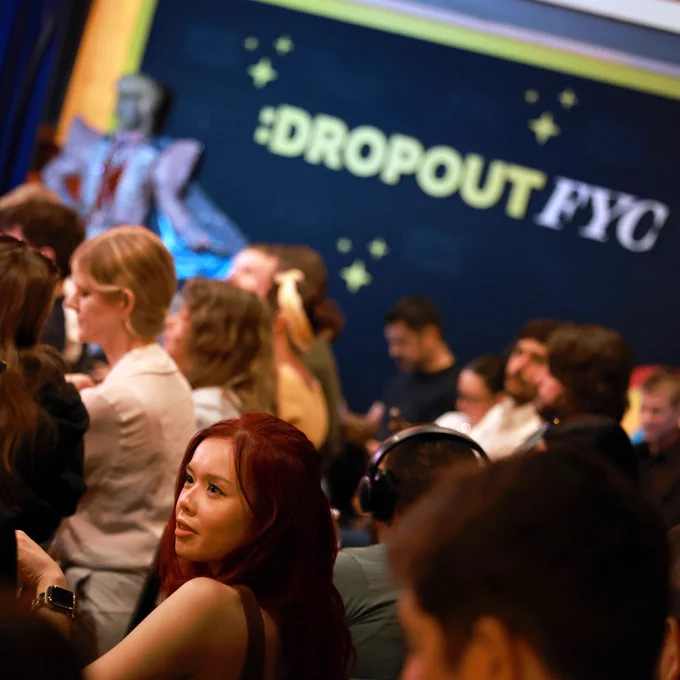 A diverse crowd gathers for the Dropout FYC event, with a focused woman in the foreground and a colorful backdrop featuring branding.