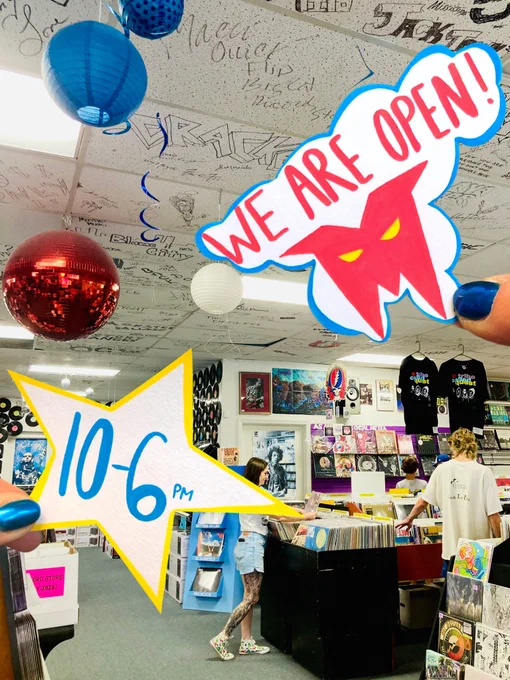 A vibrant record store scene featuring 'We Are Open' and '10-6 PM' signage against a backdrop of vinyl records and customers browsing. The atmosphere is lively and colorful.