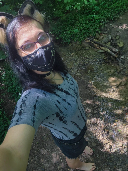 a photo of me with raccoon ears and a face mask barefoot standing in the forest 