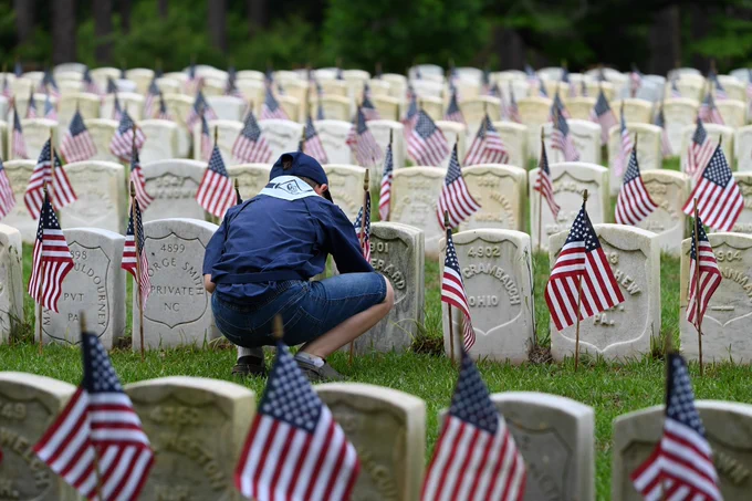 A boy scout places flags at gravestones for a Memorial Day event to honor fallen service members.