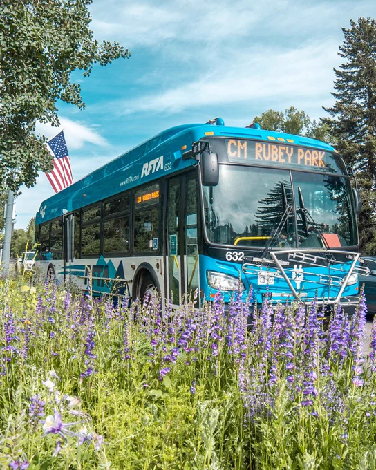 a RFTA bus drives near a field of flowers with an american flag flying in the background