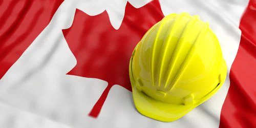 A bright yellow hard hat rests on a Canadian flag. The flag's red maple leaf and white background highlight themes of industry and national pride.