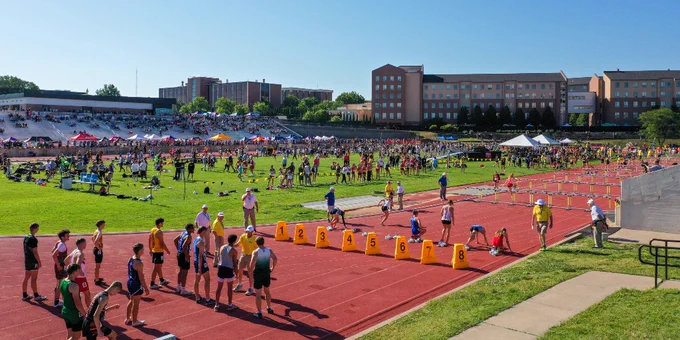 A vibrant track and field event taking place in a large stadium with numerous participants on a sunny day.