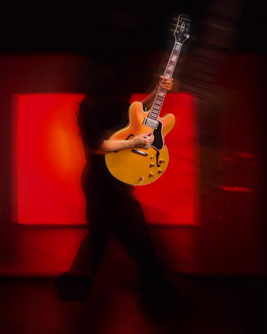 Person playing an Epiphone Futura ES-355 guitar on stage with a red-lit background.