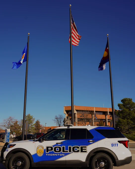 Thornton Police patrol car parked in front of three flag poles, with the American flag in the center