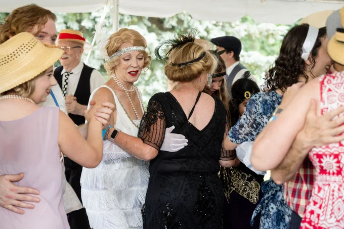 Group of people dressed in vintage attire dancing closely under a tent at an outdoor event.
