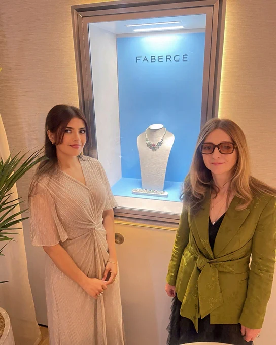Two people posing beside a Fabergé jewellery display case.