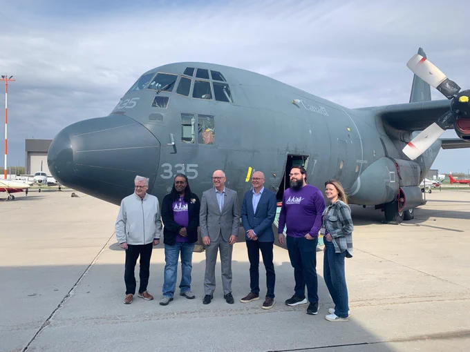 Alt text: Six people stand on an airport tarmac in front of a large grey military aircraft marked with “Canada” and the number 335. Some members of the group wear purple RRC Polytech shirts.