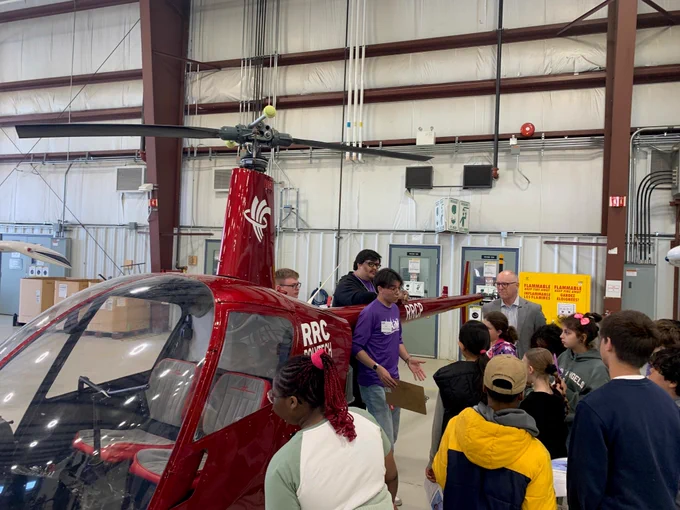 Alt text: A group of people gather around a red helicopter inside a large aviation hangar at RRC Polytech.