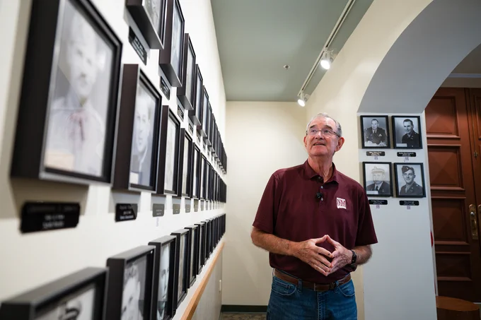 A man with glasses in an NMSU shirt looks over photos of fallen Aggie servicemen displayed at Memorial Tower