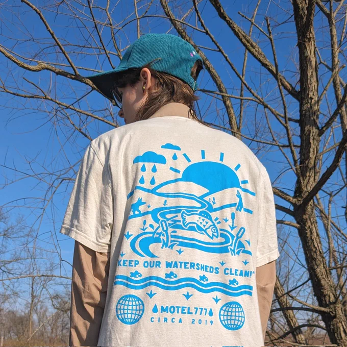 A model showing the back of the Keep It Clean tee, standing in front of a tree.