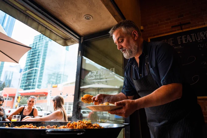 A person preparing food next to an open window facing a patio dining area. 