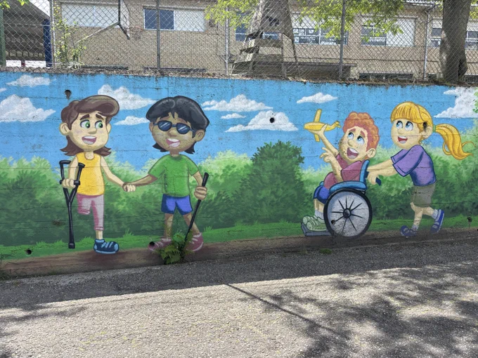 Four children on a mural. One in yellow shirt with crutch, one with glasses in a green shirt, one in wheelchair