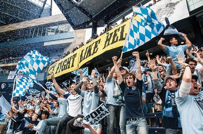 Fans cheering in a sports stadium stand.