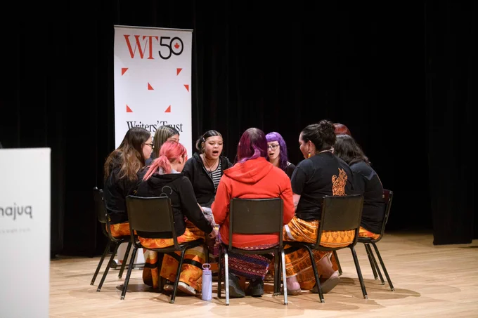 A circle of  indigenous women holding hands while sitting in a circle. 