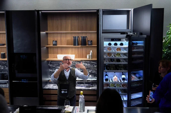 LG built-in showroom event with a presenter demonstrating premium kitchen appliances, including an illuminated LG wine cellar filled with bottles and sleek black cabinetry.