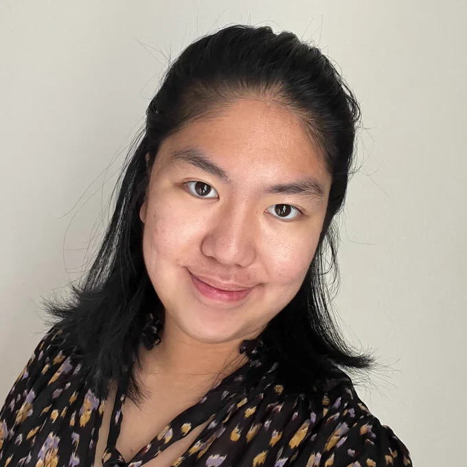 Psychology major Angela Sun wearing a dark patterned blouse against a light-colored wall.
