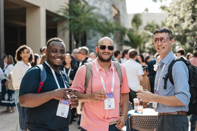Three smiling men attending an MSP Summit networking event holding up drinks and smiling for the camera.