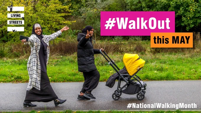 Two women joyfully walking on a path, one pushing a stroller with a bright yellow cover, surrounded by green trees.