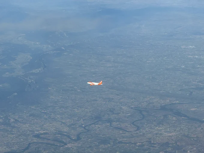 A white and orange Easyjet Airbus crossing right to left below us. The northern Spanish countryside in the background, still fairly green in late spring.