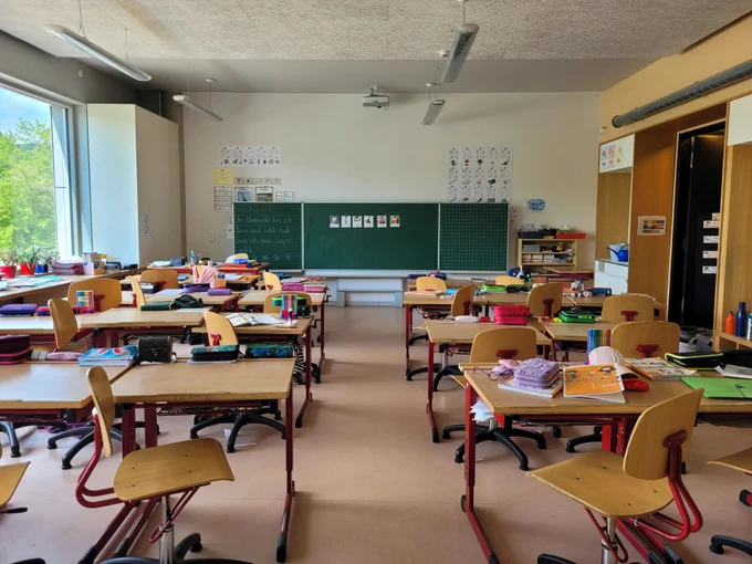Classroom view with rows of student desks and chairs facing a green chalkboard. 